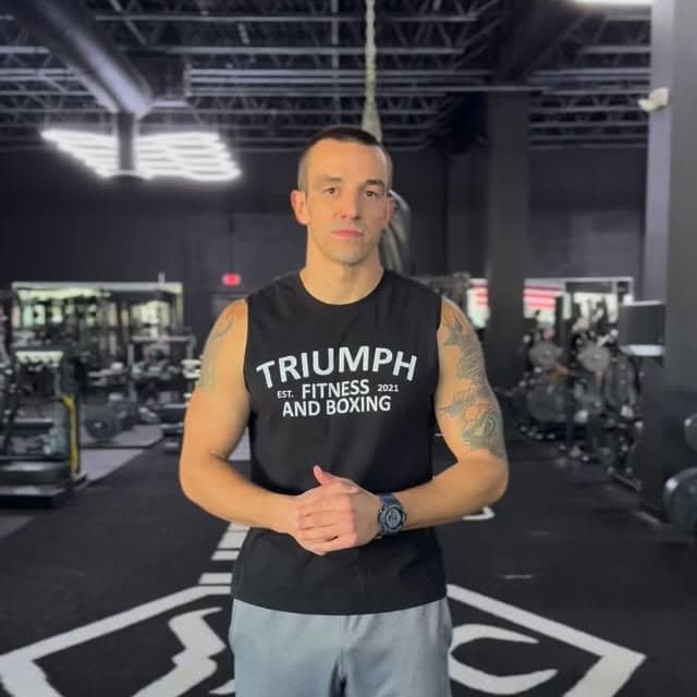 Eric Lawes standing in the gym in a Triumph Fitness and Boxing shirt