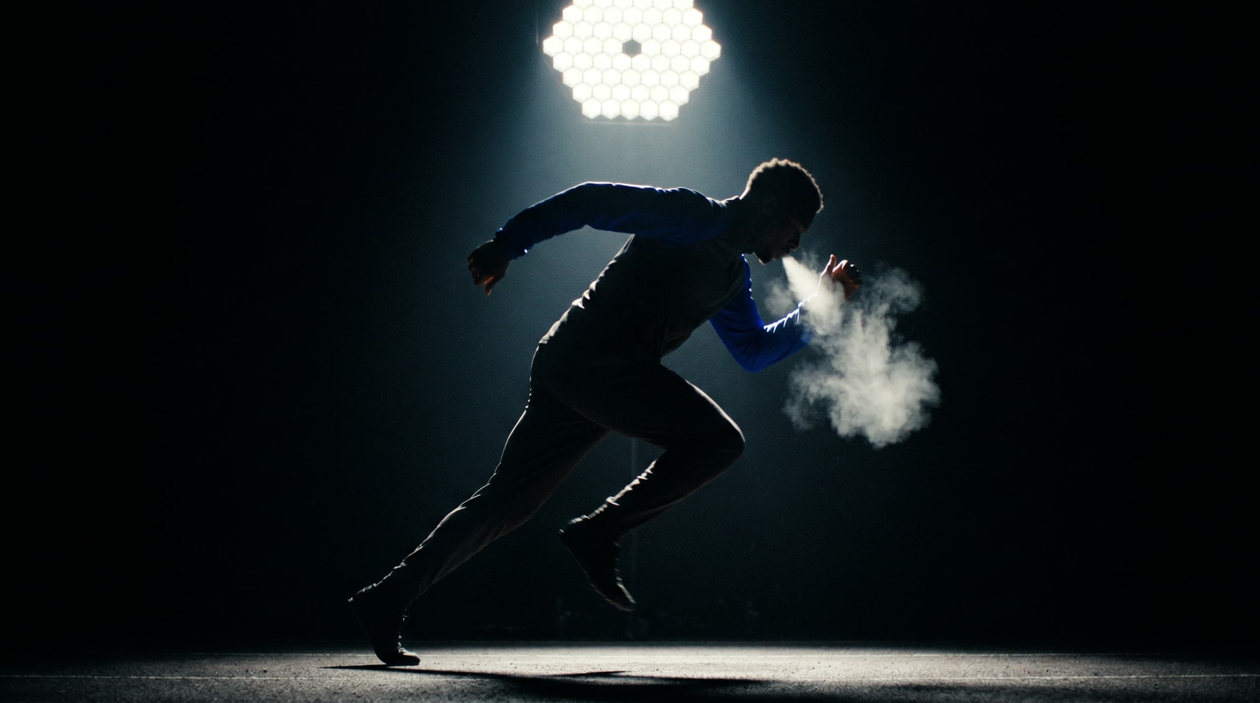 Silhouette of an athlete sprinting through a pool of light, breath vapor glowing